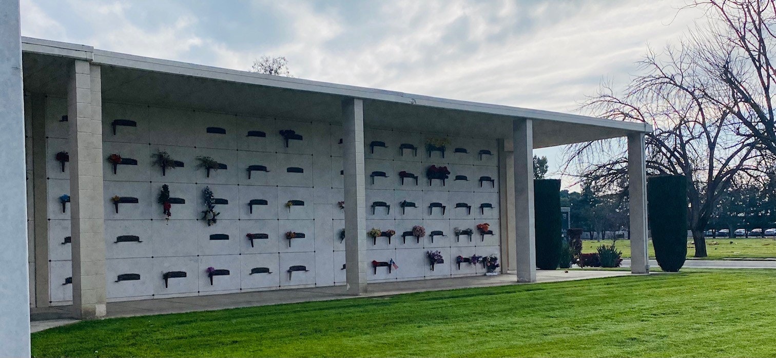 A columbarium wall with niches adorned with flowers at a cemetery.