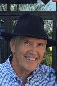 A smiling person wearing a black hat and a checkered shirt.