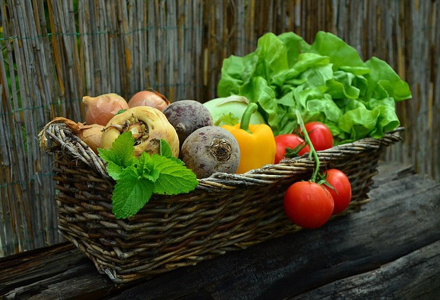 A basket of fresh vegetables including lettuce, tomatoes, and peppers on a wooden surface.