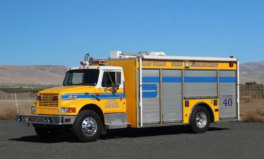 Yellow fire truck parked outdoors with clear skies.