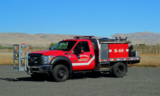 A red fire truck with "B-40" on the side, parked in a field under a clear blue sky.