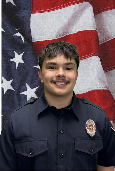 A person in a uniform posing in front of an American flag backdrop.