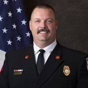 A firefighter in uniform with badges in front of the American flag.