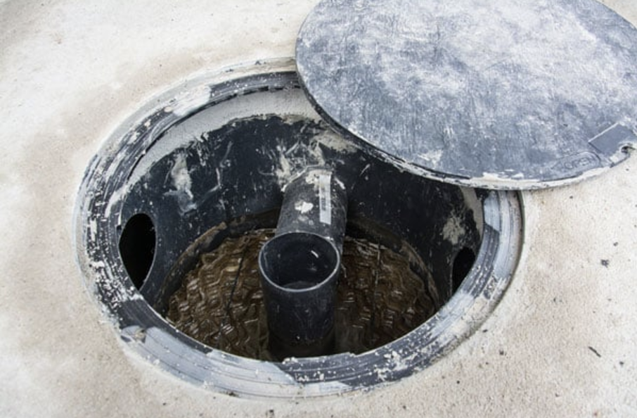 An open manhole with a partially displaced cover and visible pipes.