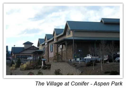 Buildings with peaked roofs, parking lot, and some vegetation at The Village at Conifer - Aspen Park.