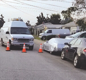 A white van, traffic cones, and parked cars on a residential street.