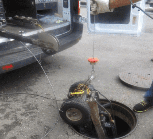 A small wheeled device is being hoisted from a manhole using a cable attached to a truck.