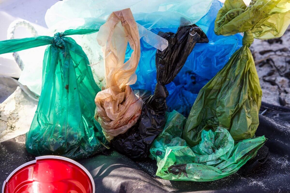 Colorful, tied plastic bags filled with waste, alongside a red container, on a surface with scattered debris.