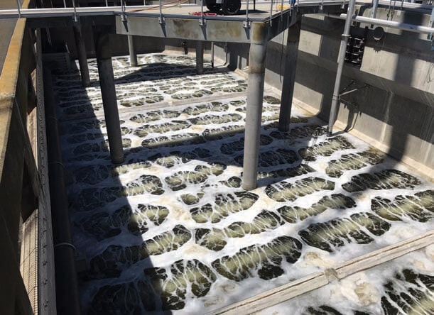 A wastewater treatment aeration tank with bubbling water and foam, used for biological treatment.