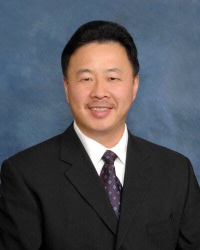 A person in a suit and tie smiling against a blue background.