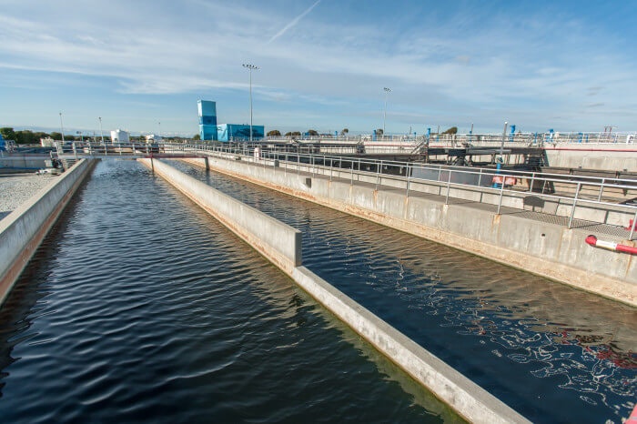 A water treatment facility with long concrete channels filled with water under a clear sky.