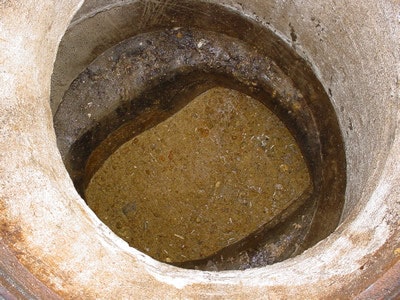 A close-up view of a dry, empty well with a rough, circular border and soil at the bottom.