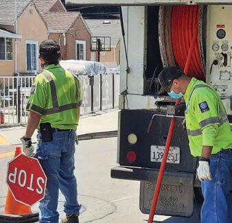 Two workers in safety vests working near a truck; one holds a stop sign, the other is near equipment.