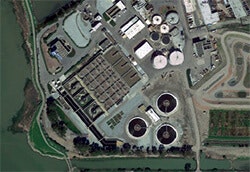 Aerial view of an industrial facility with tanks, walkways, and surrounding greenery, possibly a wastewater treatment plant.