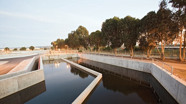 A wastewater treatment facility with a large water channel, surrounded by trees and pathways.