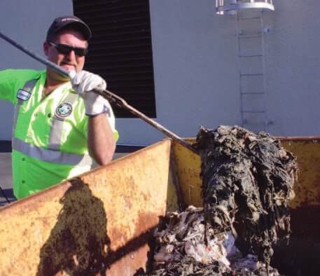 Worker in safety gear cleaning waste from a bin with a long tool.