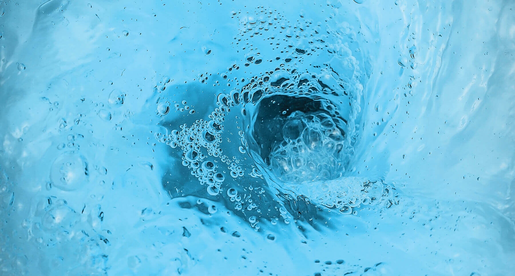 Blue swirling water with bubbles forming a vortex.