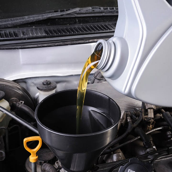 Motor oil being poured into a funnel in a car engine.