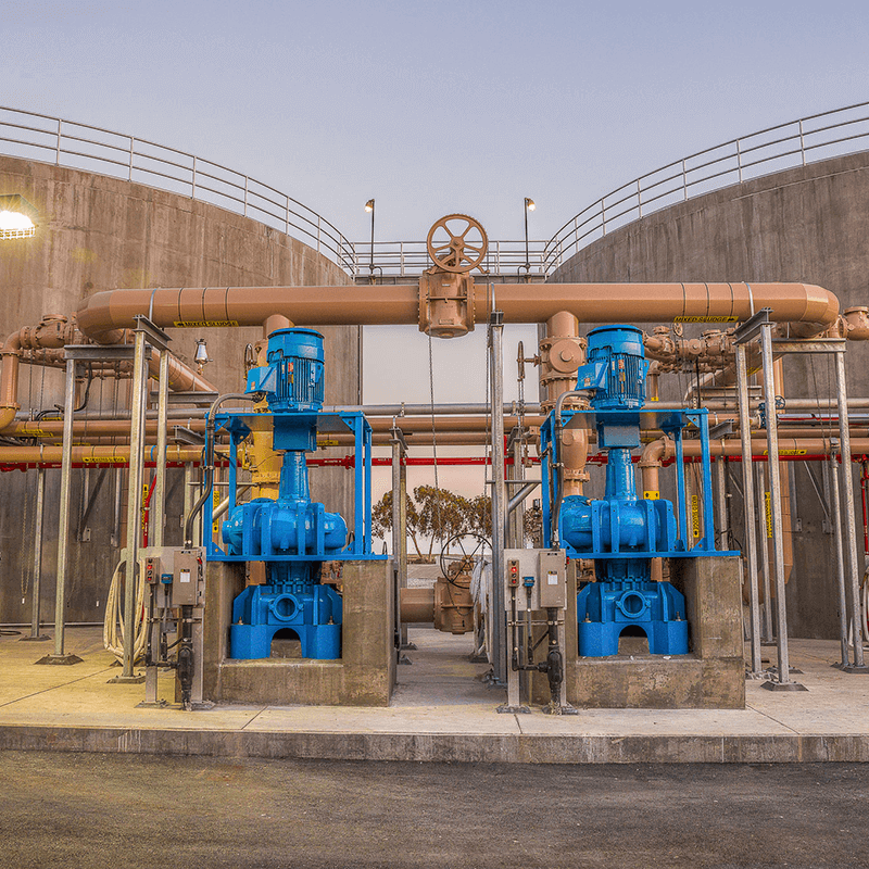 Industrial equipment with blue pumps and large pipes outside a concrete structure.