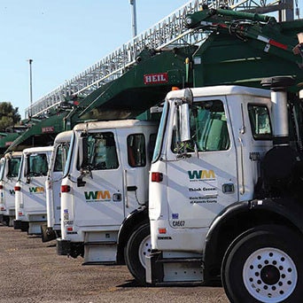 A row of white waste management trucks lined up with green equipment on top.