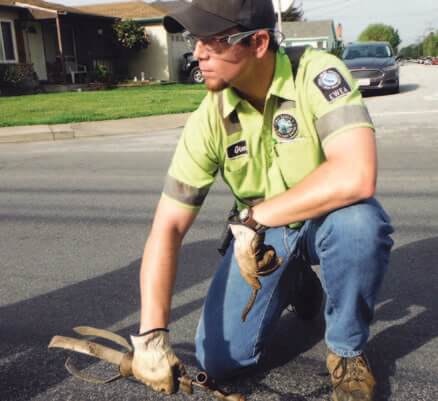 A person in a uniform, crouching on a street, working with tools.