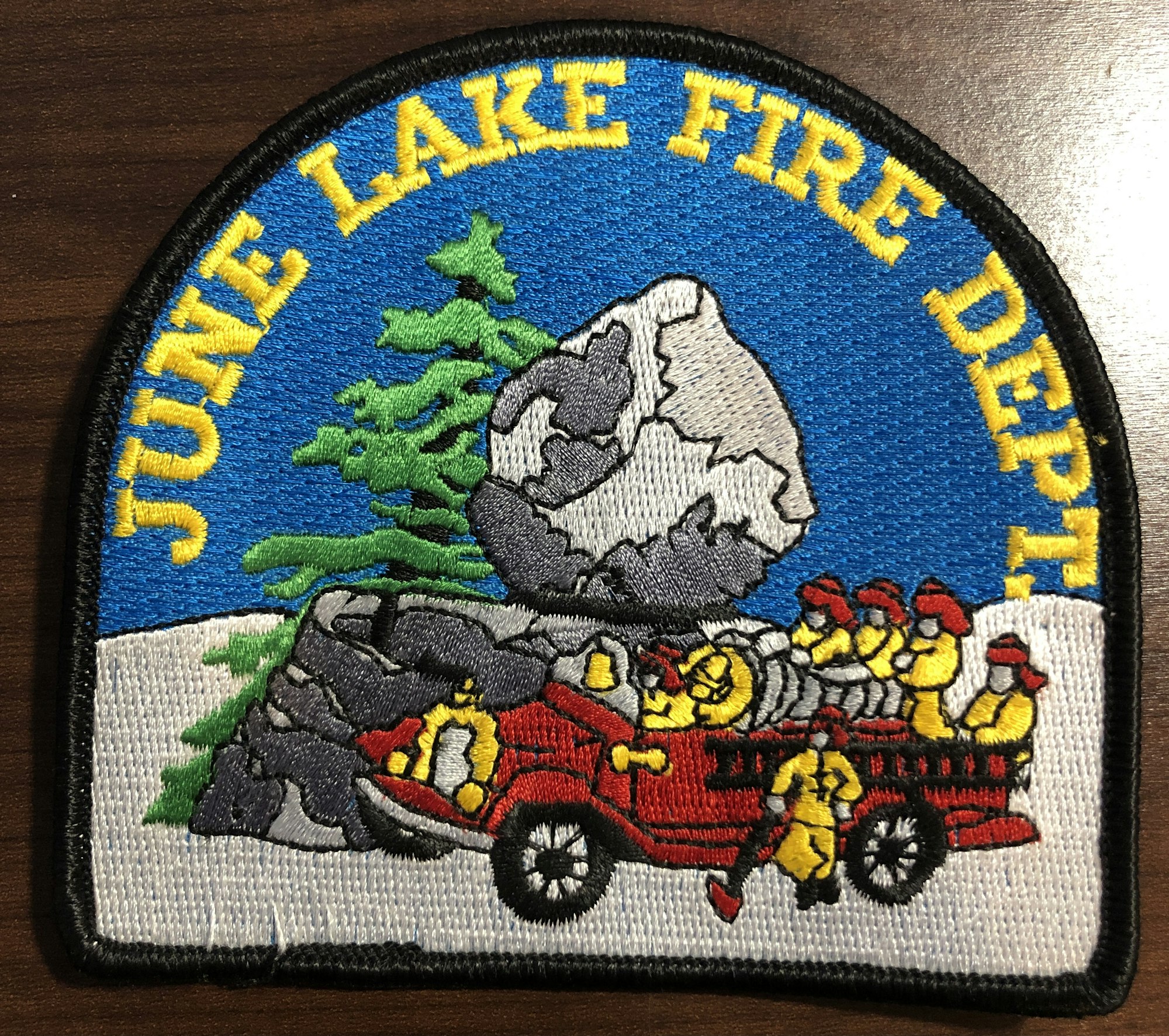 Patch of June Lake Fire Dept. featuring firefighters, a red fire truck, a boulder, and trees.