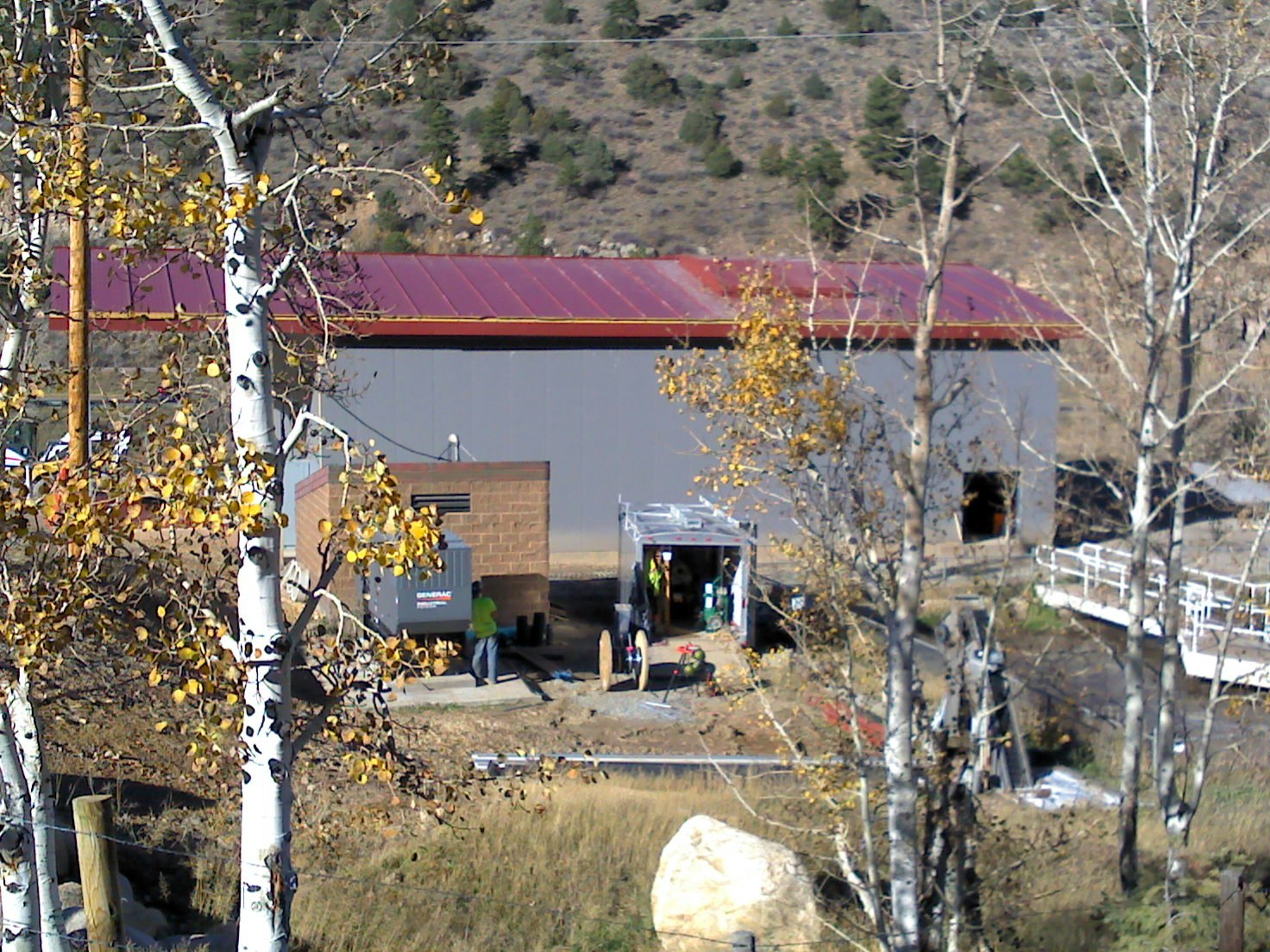 A building with a red roof, trees with yellow leaves, people working outside, and construction equipment.