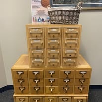 Wooden card catalog with multiple drawers, a basket on top.