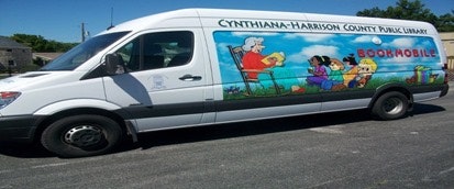 A library bookmobile van with colorful illustrations and text "Cynthiana-Harrison County Public Library."