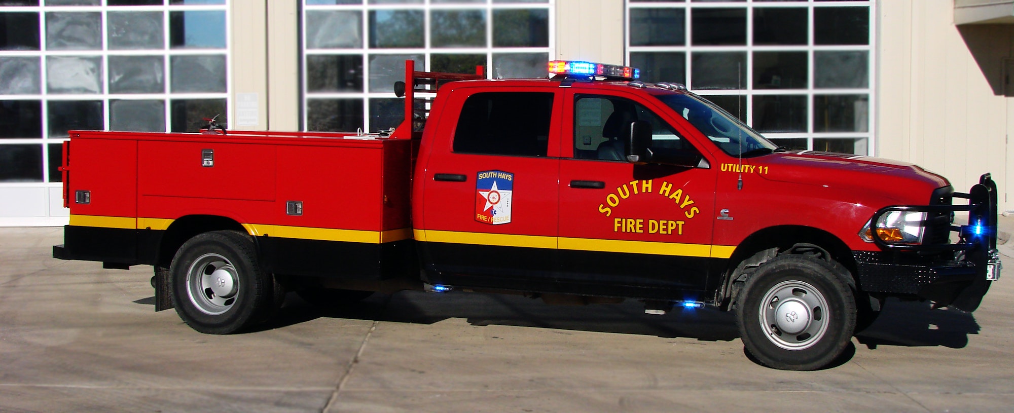 A red fire department utility truck with lights on and logo, parked in front of a building with large windows.
