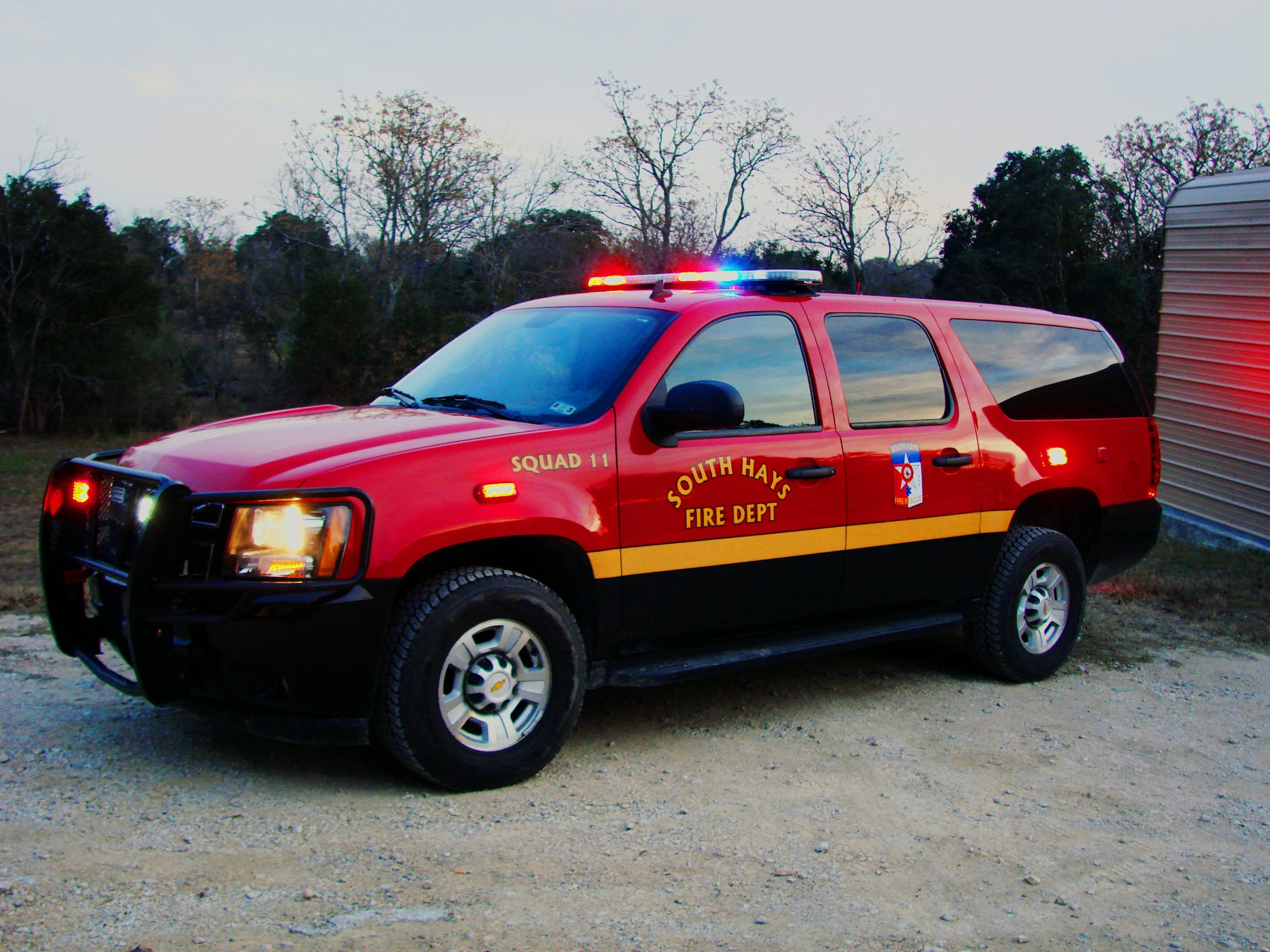 A red fire department SUV with lights on, labeled "SQUAD 11 SOUTH HAYS FIRE DEPT".