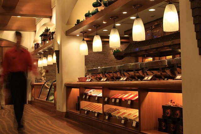 A cozy restaurant interior with warm lighting, serving stations, and a blurred waiter in a red shirt walking by.