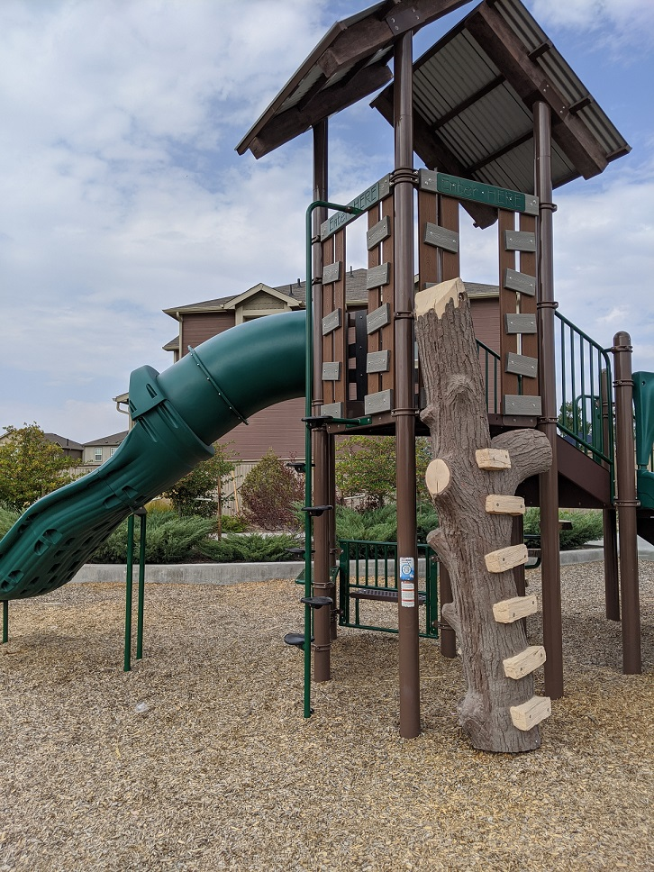 A playground featuring a green slide, climbing structure, and a log for kids to climb.