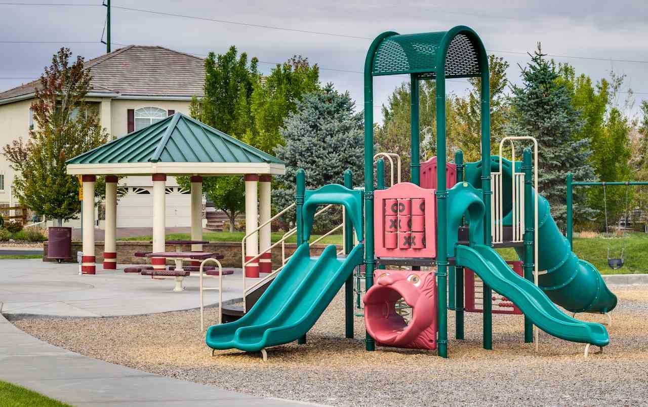 A colorful playground with slides and a gazebo amidst greenery.