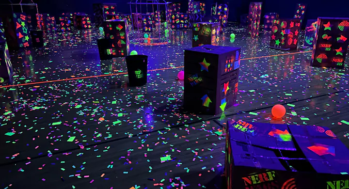 Glowing neon-lit arena with scattered balls and confetti, featuring obstacles for an indoor game like laser tag or Nerf.