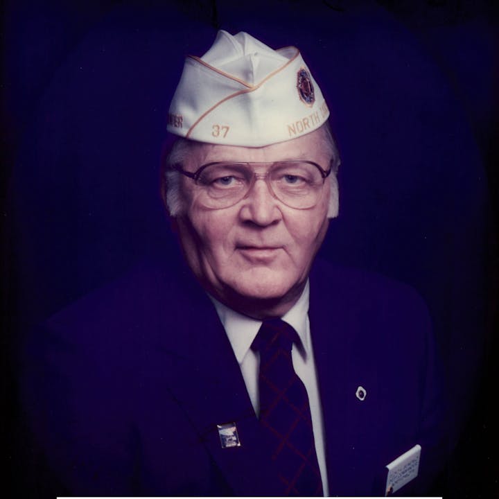Portrait of a man in glasses wearing a service cap and suit with badges and a tie.