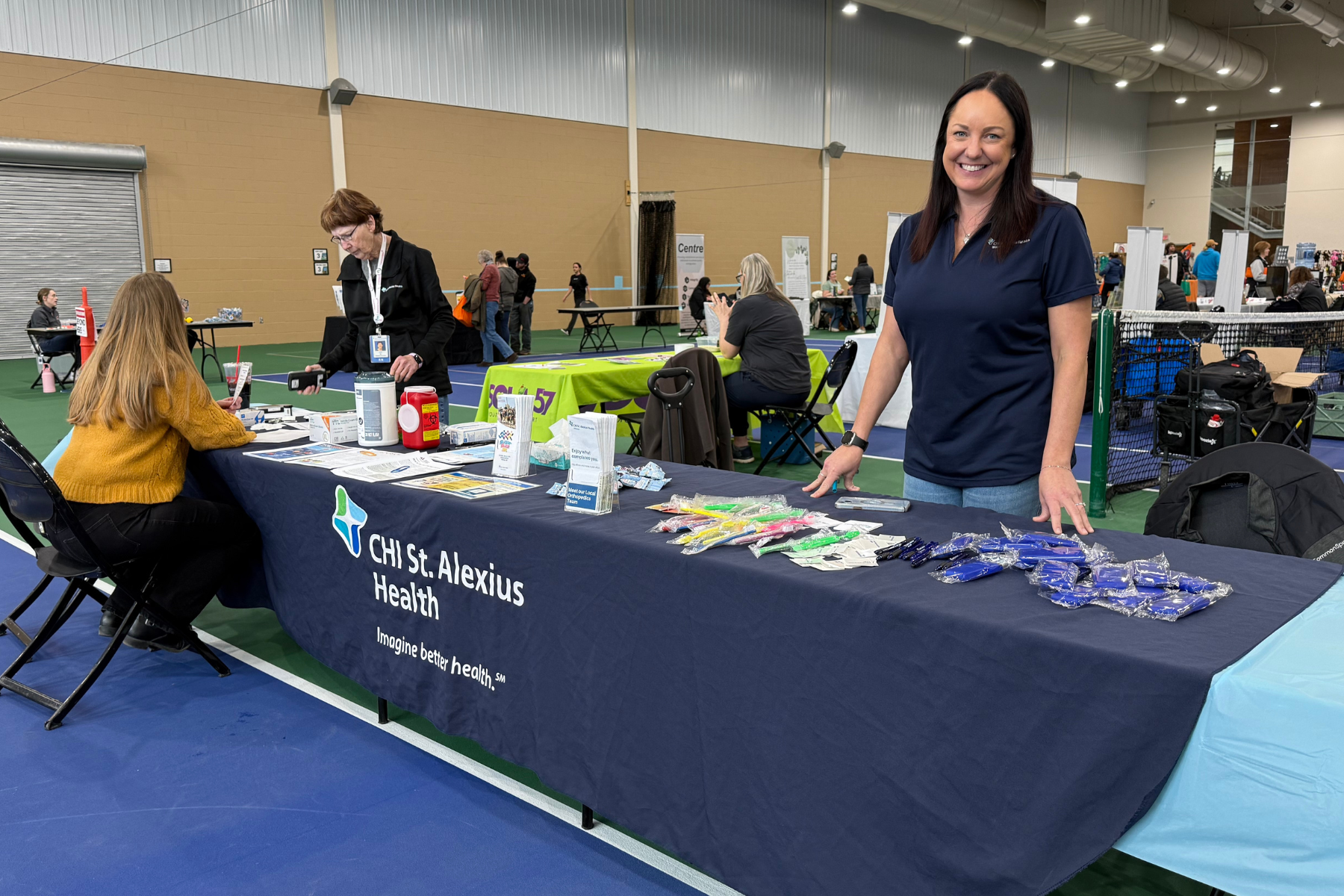 A woman stands at a CHI St. Alexius Health booth, showcasing health resources and promotional items at an event.