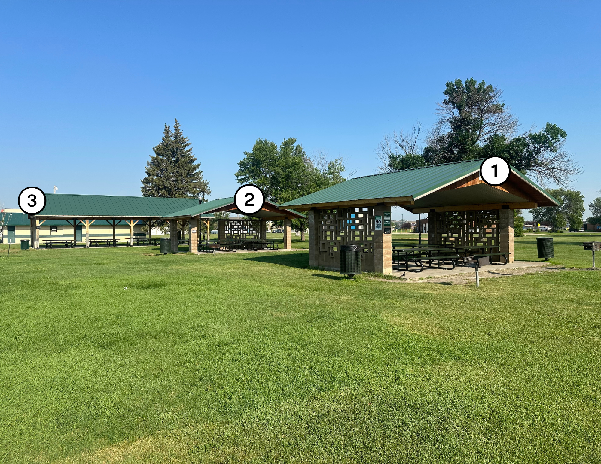 The image shows three picnic pavilions in a park, with green grass and a clear blue sky. Each pavilion is labeled with numbers.