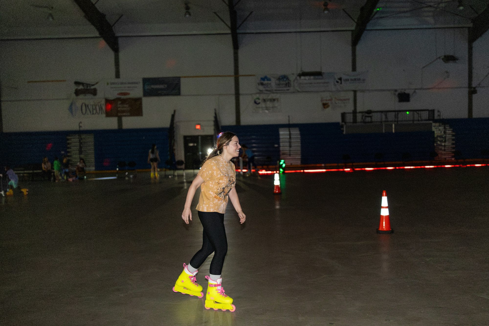 Person roller skating indoors with bright yellow skates, passing an orange cone, in a dimly lit rink.