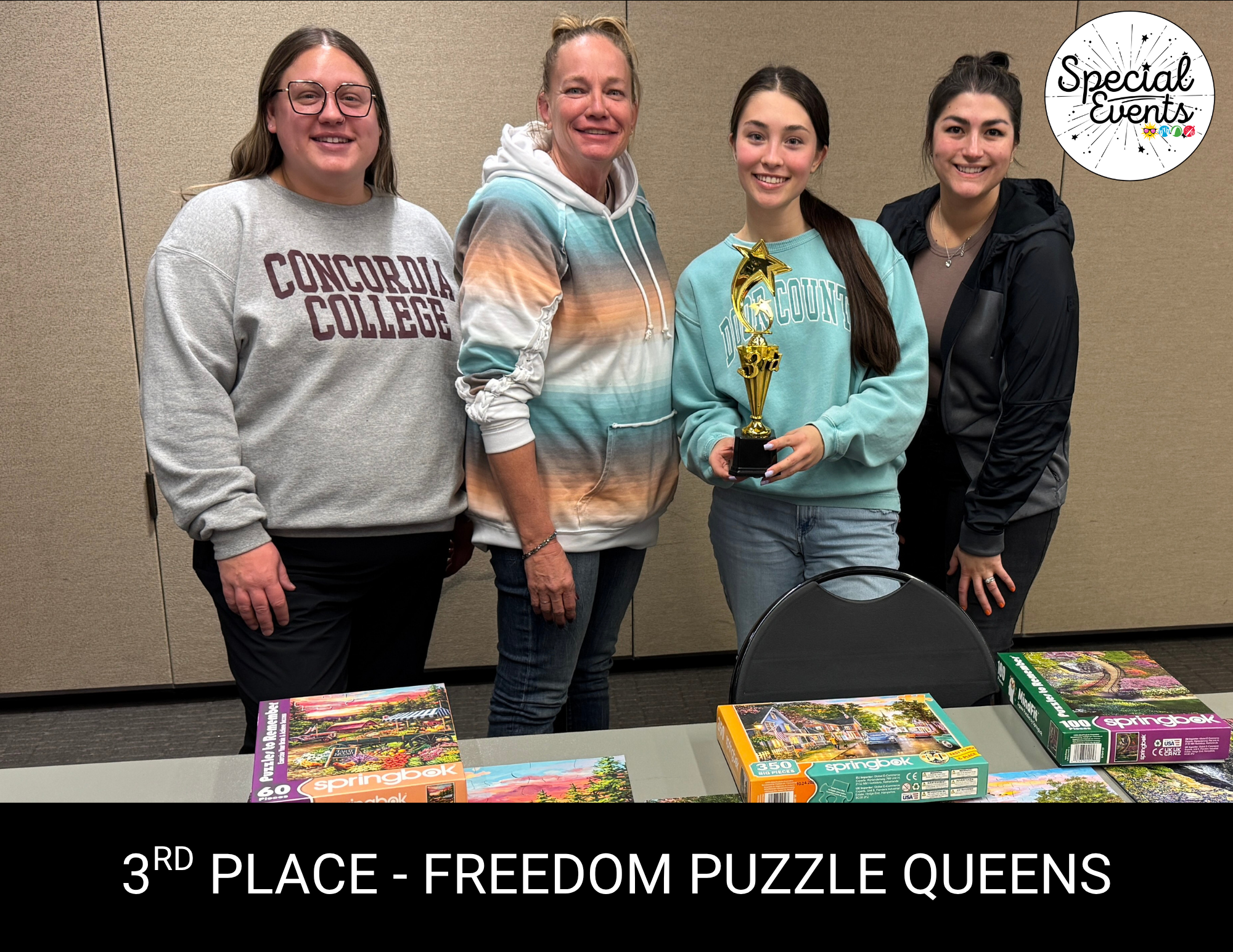 A group of four women pose with a trophy for "3rd Place - Freedom Puzzle Queens" alongside jigsaw puzzles on a table.