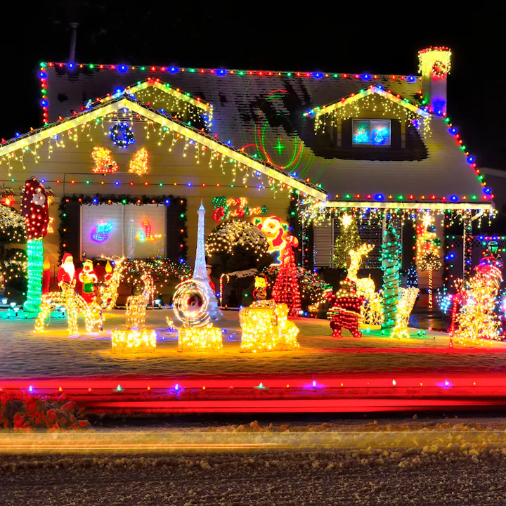 A house adorned with colorful Christmas lights and decorations, including inflatable figures and a lit-up front yard.