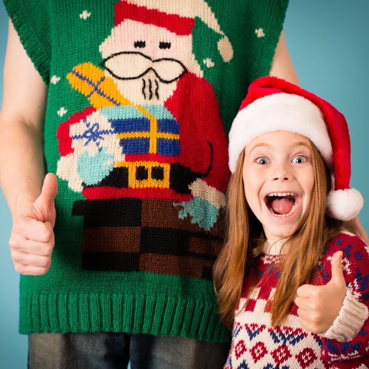A child in a Santa hat gives a thumbs-up next to an adult in a festive Santa sweater.