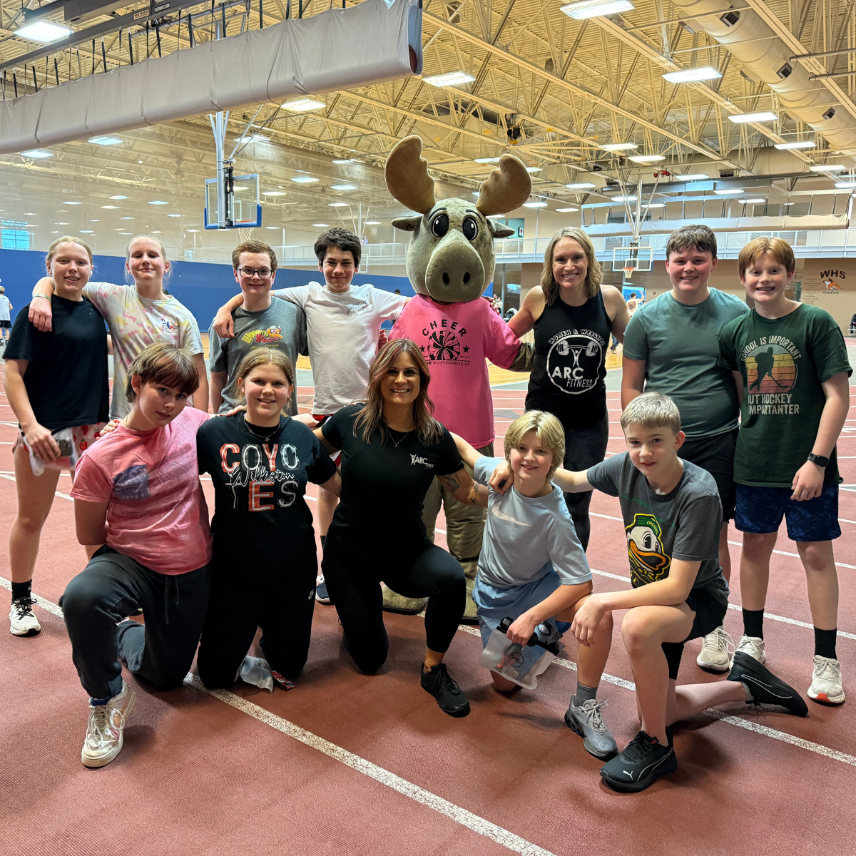 A cheerful group of kids and adults poses with a moose mascot in a gym, promoting fun and fitness activities.