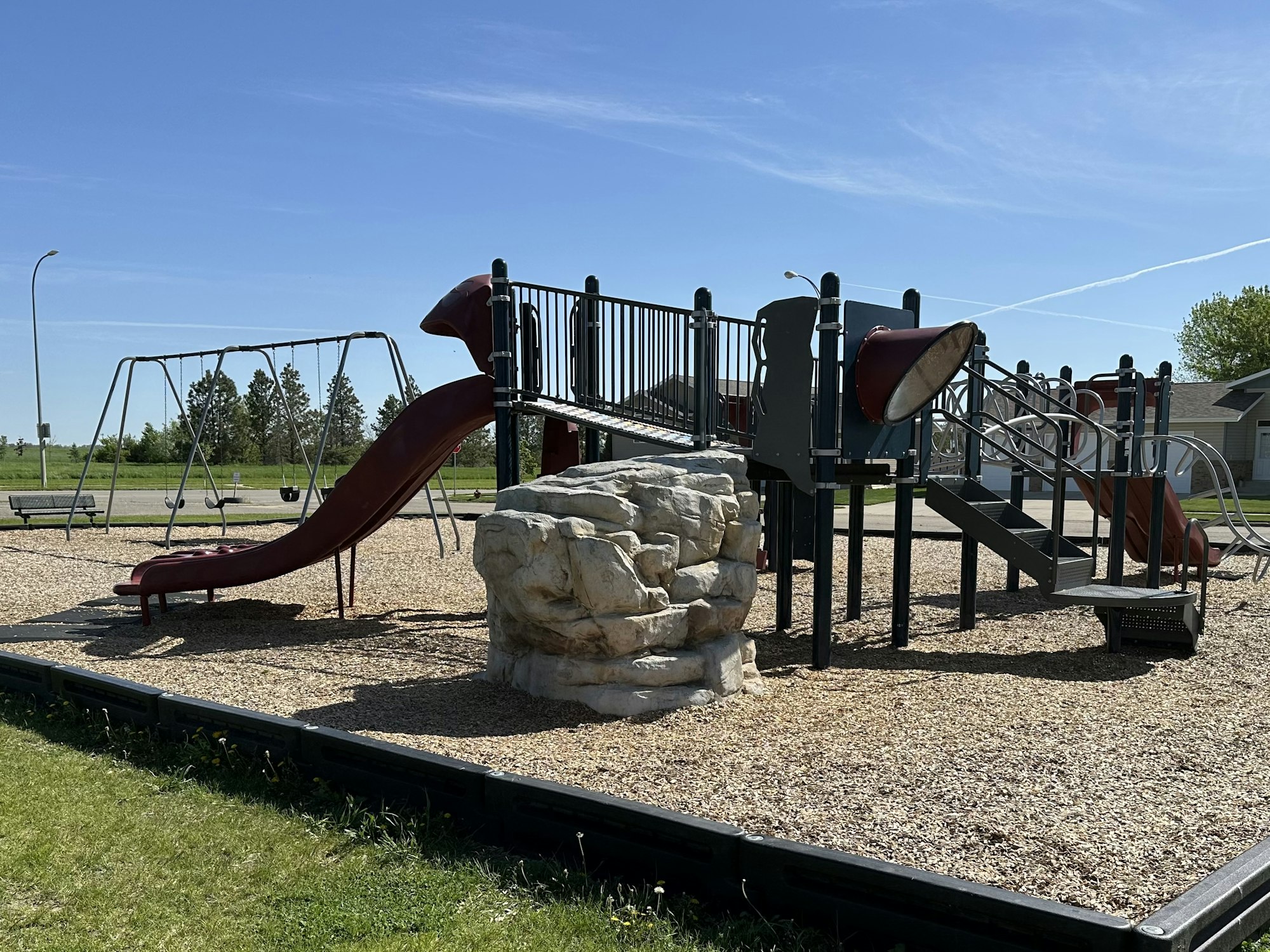 Playground with slide, swings, climbing structure, and blue sky.
