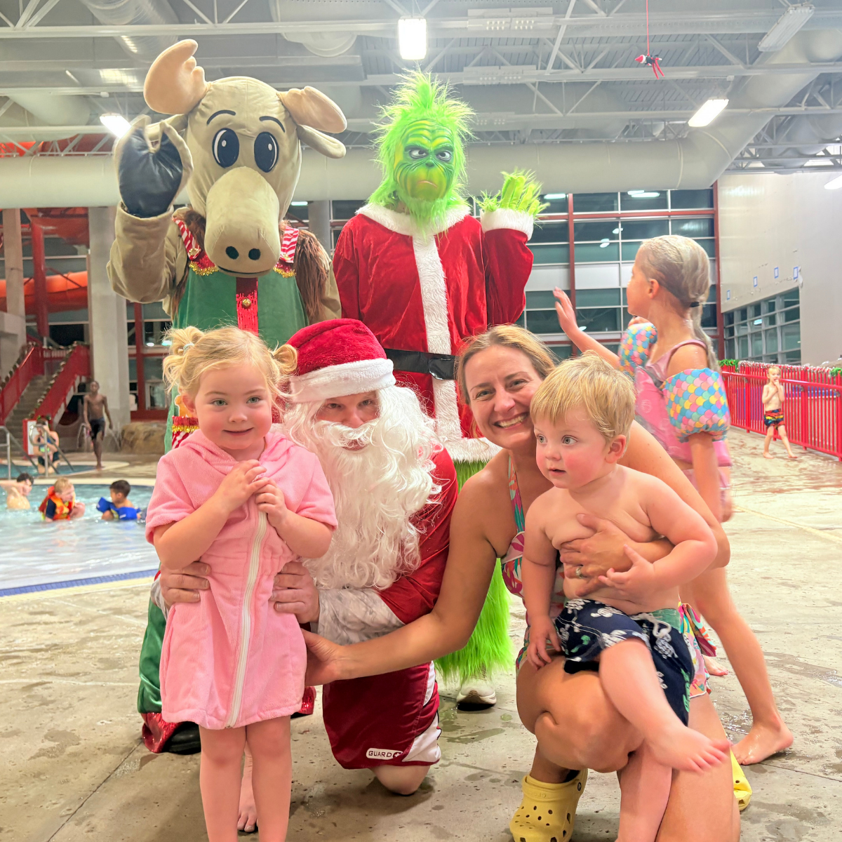 A festive scene with kids, Santa, the Grinch, and a moose mascot at a pool, enjoying a holiday celebration.