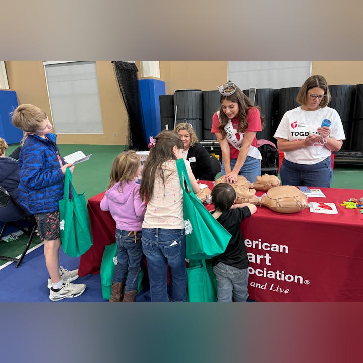 Children engage in CPR training with educators and volunteers at an American Heart Association event, promoting health education.