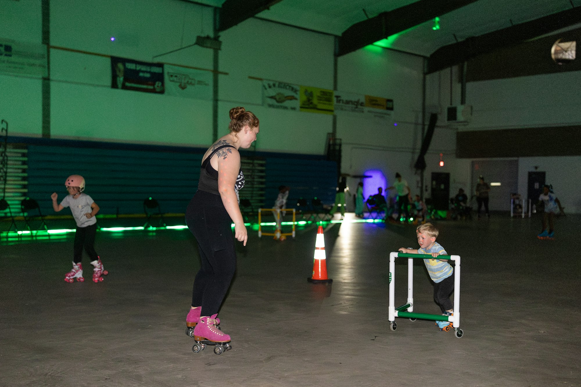 People roller skating indoors; a child uses a support frame.