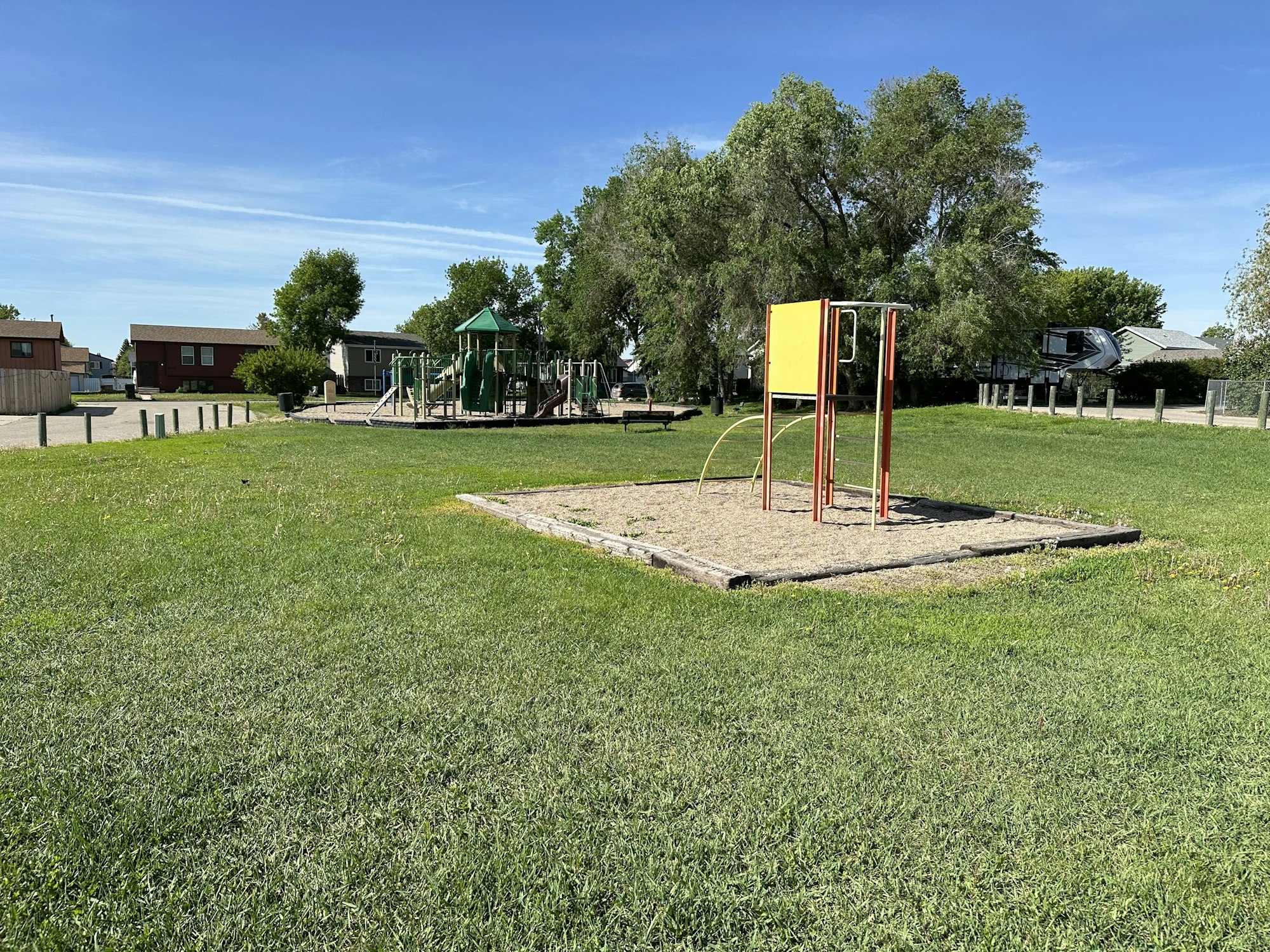 A playground with greenery, play structures, a slide, and a sandpit on a sunny day.