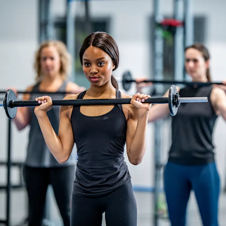 A group of women exercising in a gym, lifting barbell weights, showcasing strength and fitness.