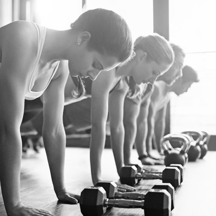 People exercising with dumbbells and kettlebells in a gym setting.
